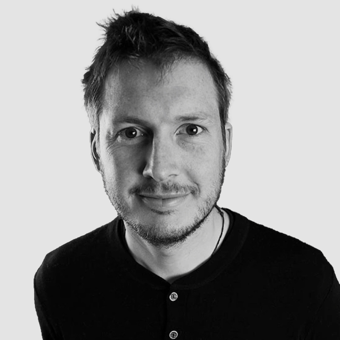 Svart hvitt profilbilde av en person med mørk genser litt skjegg og kort hår. Foto: Benjamin Richards