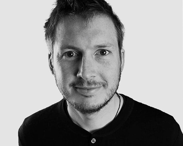 Svart hvitt profilbilde av en person med mørk genser litt skjegg og kort hår. Foto: Benjamin Richards