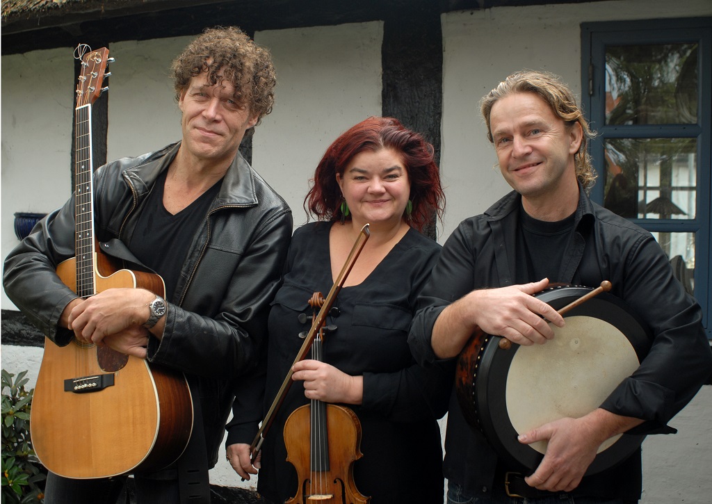 Dei tre musikarane frå bandet Tradish står og held kvart sitt instrument, gitar, fele og irsk tromme.